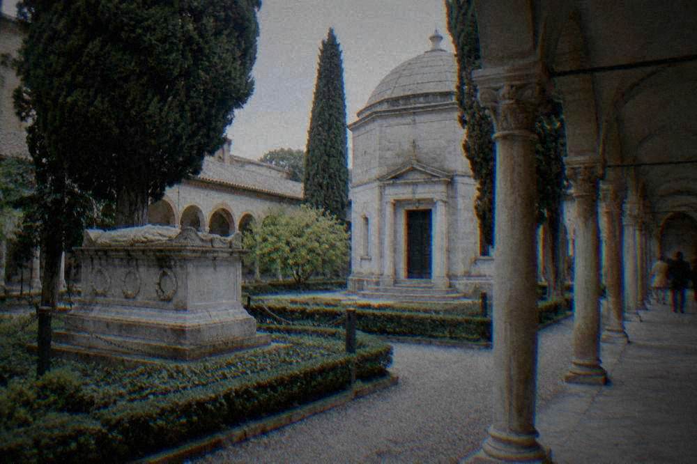 A covered arcade garden with stone memorial plaques beside a mausoleum in Ravenna