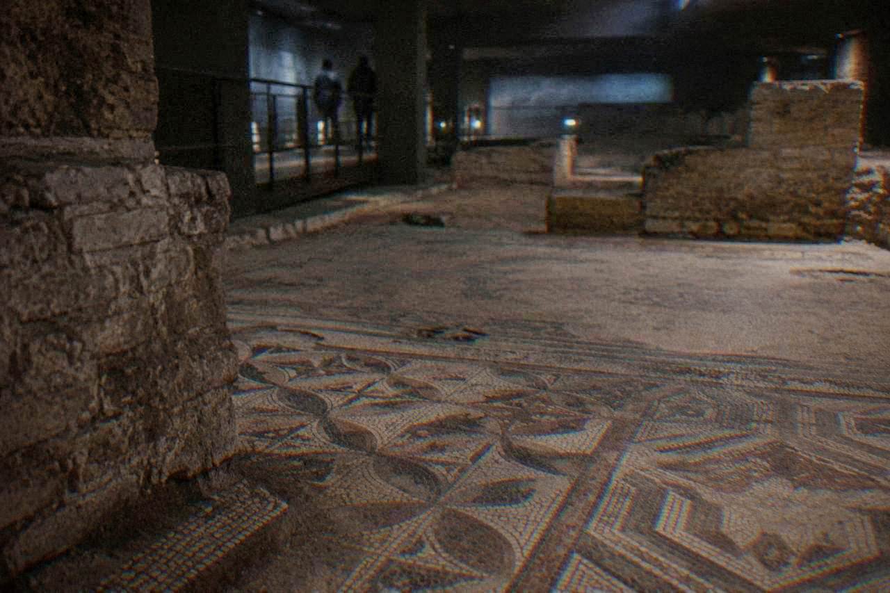 Ancient stone mosaic floor with geometric patterns inside a dimly lit underground gallery