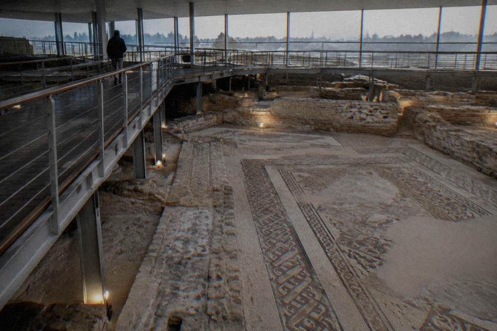 Walkway above an excavated mosaic floor with patterned borders under conservation lighting