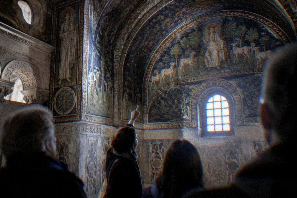 A guide pointing out mosaic details to a small group in a Ravenna church interior