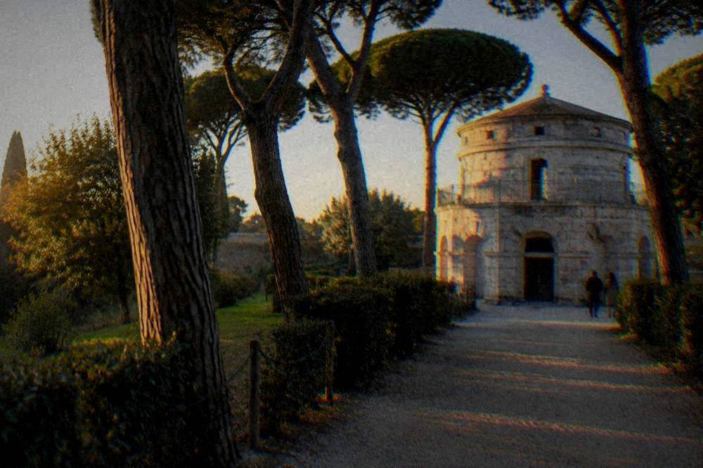 A tree-lined gravel path leading through the park toward the round stone mausoleum
