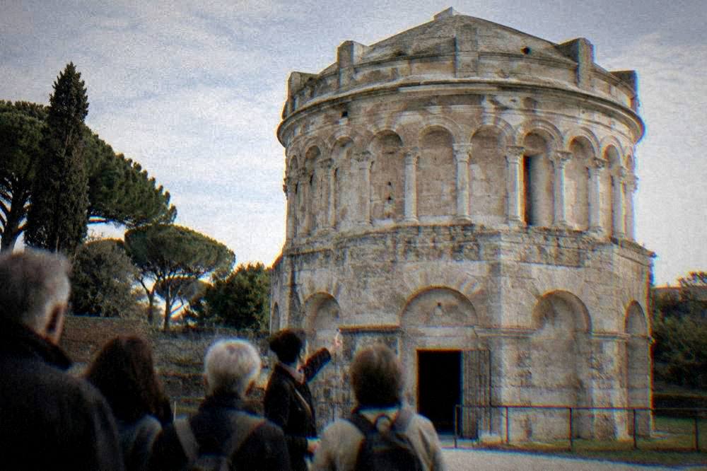 A guide pointing out the carved arcading on the upper drum of the mausoleum to a small group of visitors