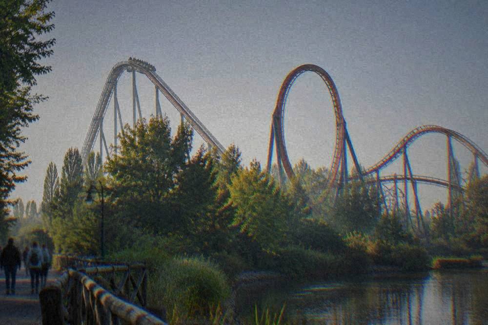 Roller coaster track looping above trees at an amusement park on a clear day