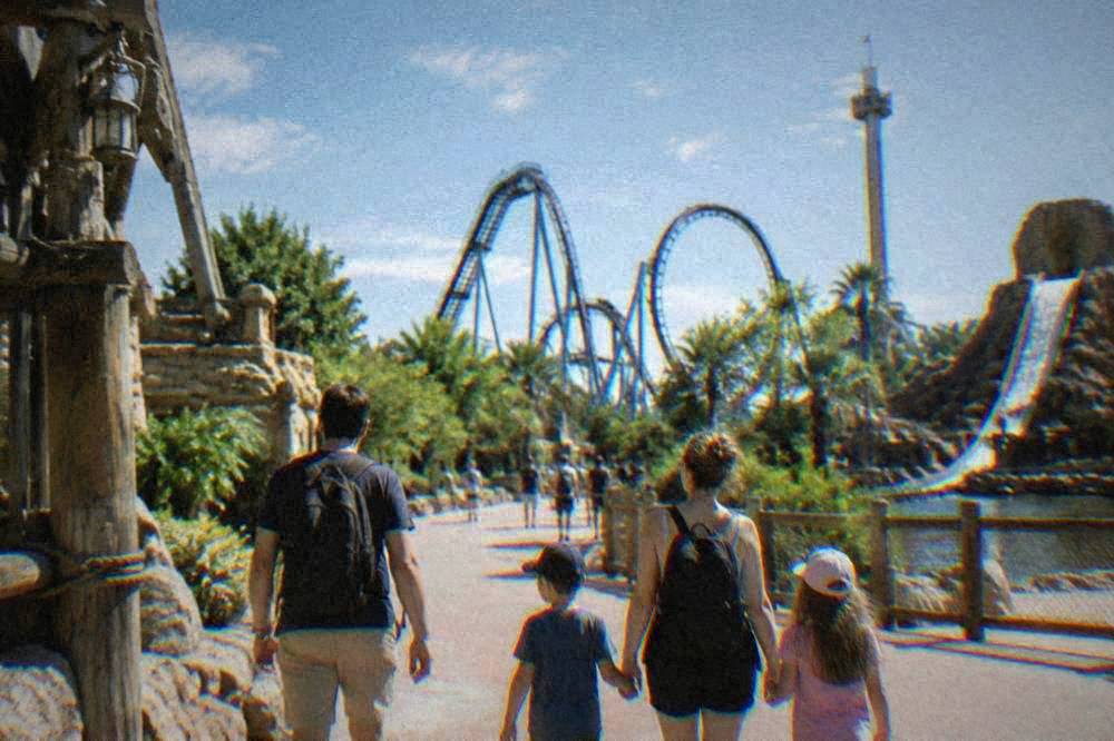 Family walking down a themed amusement park street with ride structures in the background