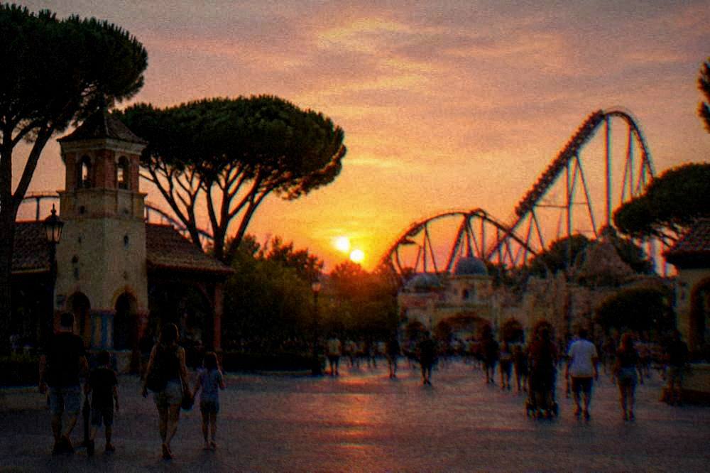 Amusement park entrance plaza with flags and families walking in early evening light