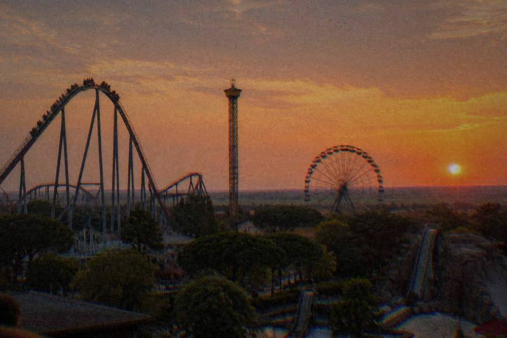 Wide view of amusement park rides against a sunset sky over flat countryside