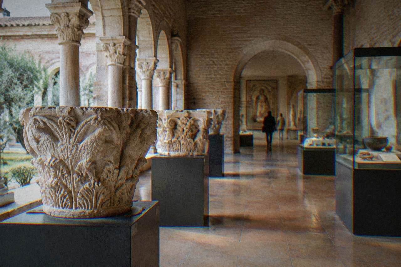 Museum gallery with stone capitals and display cases inside a historic cloister building