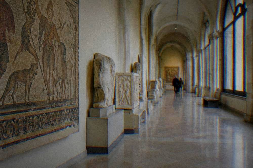 Sunlit museum corridor with arched windows and stone floors