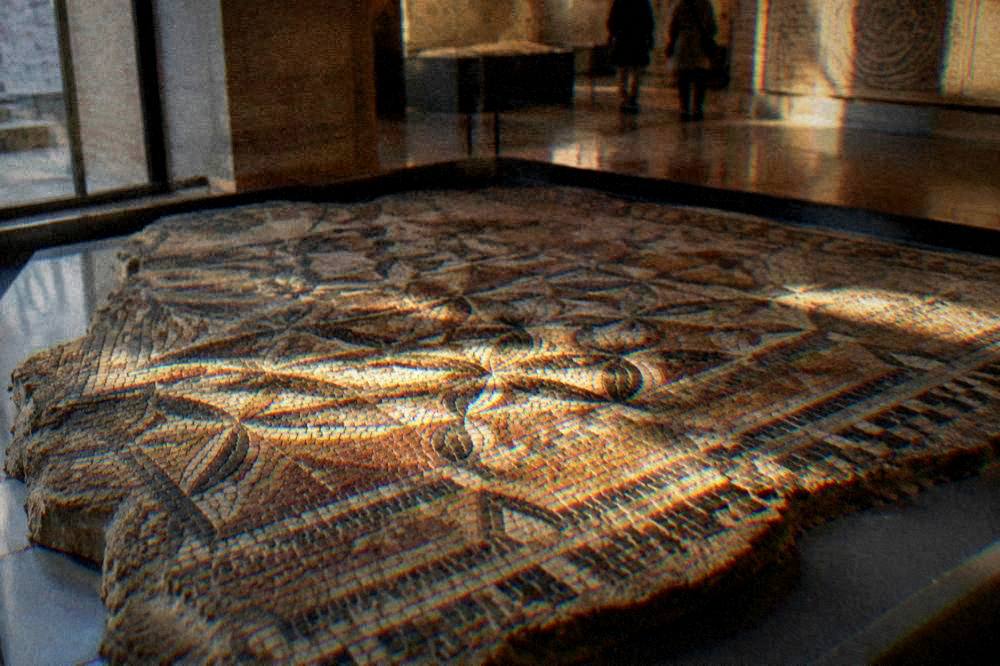 Ancient mosaic floor fragment with geometric patterns in a museum case