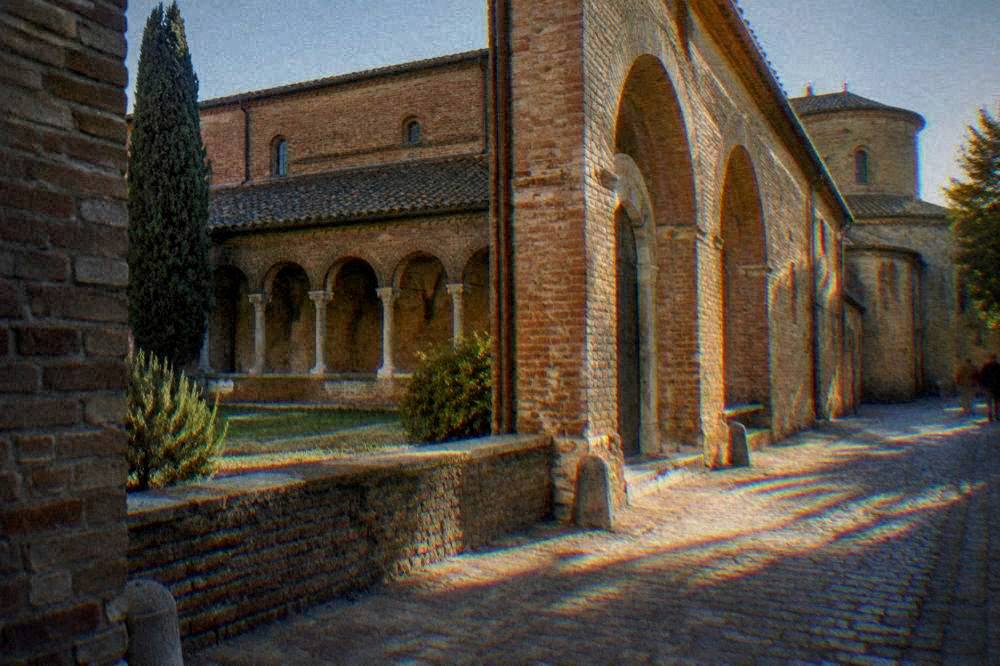 Exterior of a brick cloister building with arched doorways in an Italian street