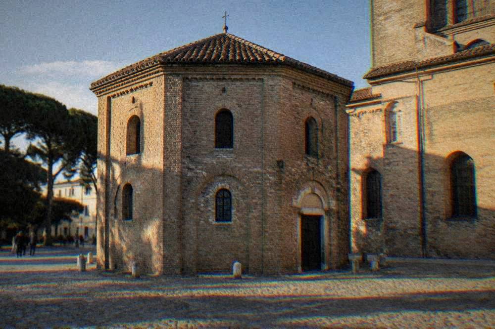 Exterior of a small octagonal brick baptistery beside a church in an Italian square