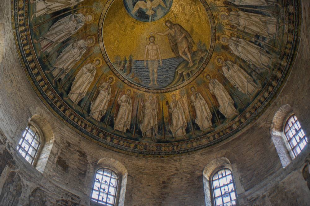 A guide speaking to a small group inside a mosaic-decorated historic building