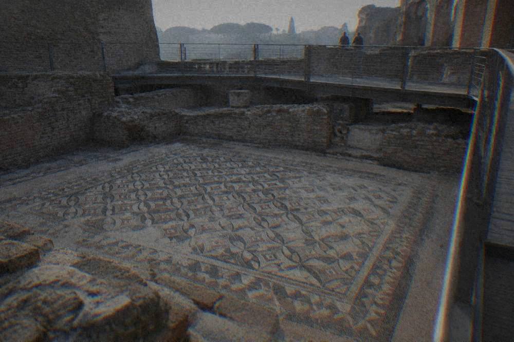 A geometric mosaic floor panel inside a lowered excavation, viewed from a modern walkway