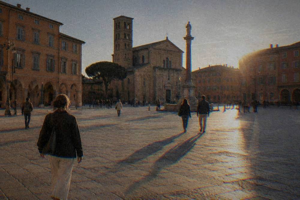 People walking across a sunlit Italian square with ochre and terracotta facades