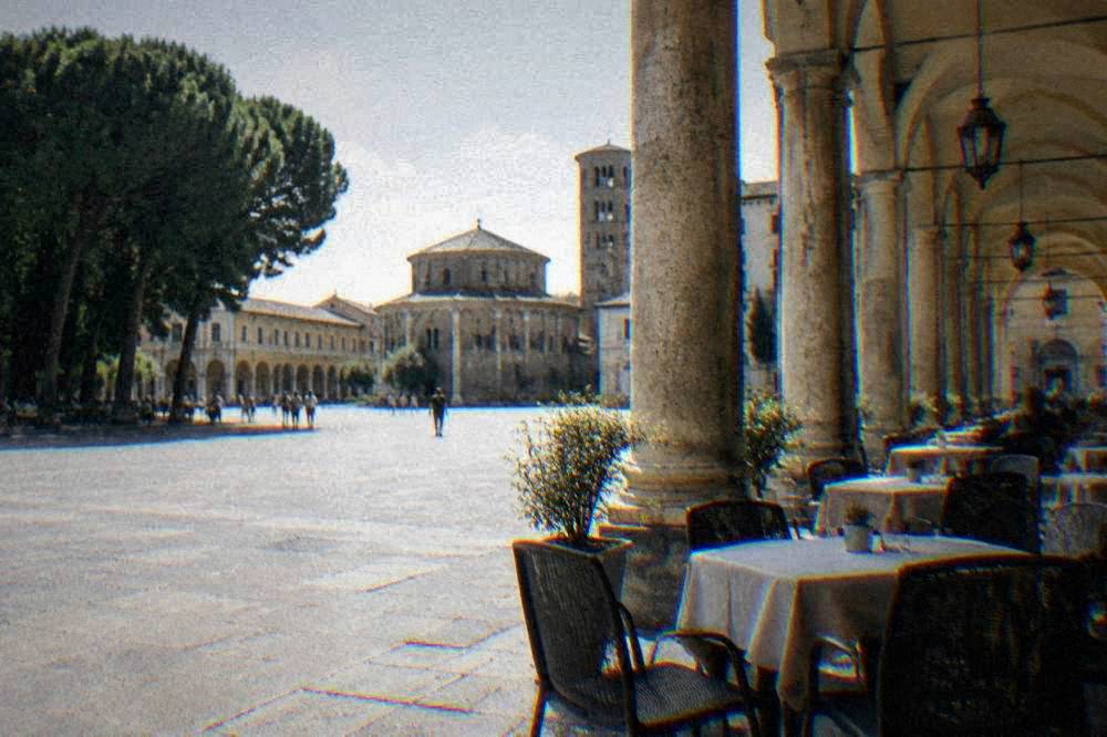 Cafe tables with chairs under the arcades of an Italian square in the late afternoon