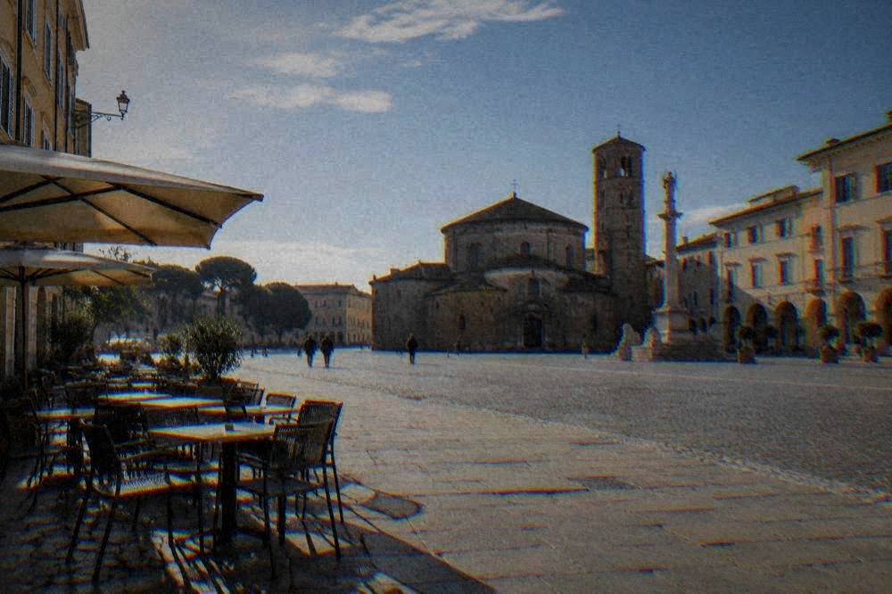 An Italian square in early morning light with empty cafe chairs and long shadows