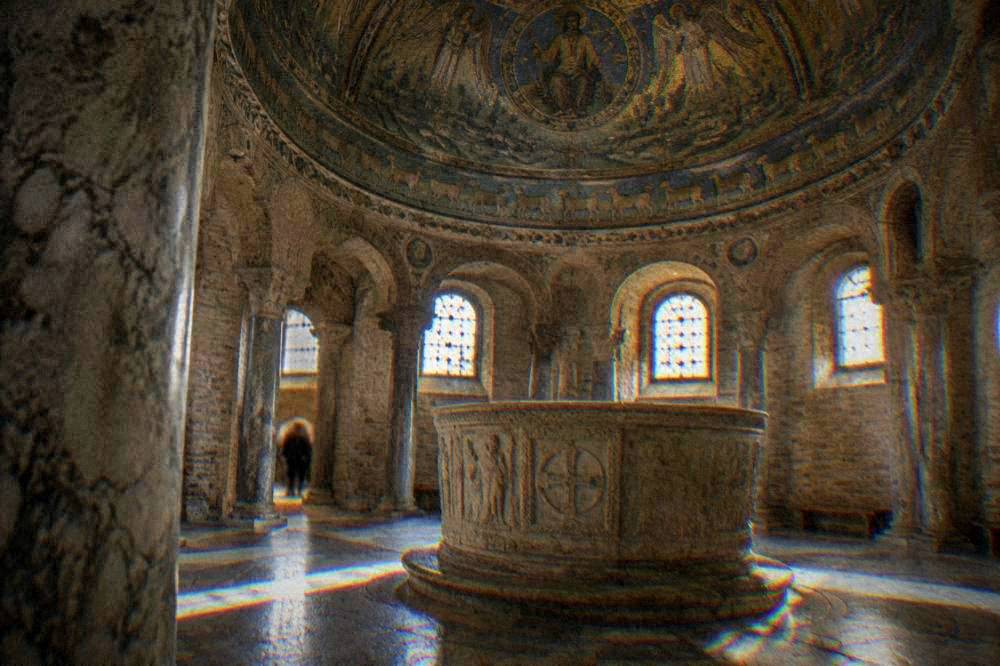 A stone baptismal font under a domed mosaic ceiling in an early baptistery