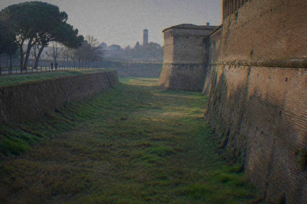 A grassy dry moat running along the base of a high brick fortress wall