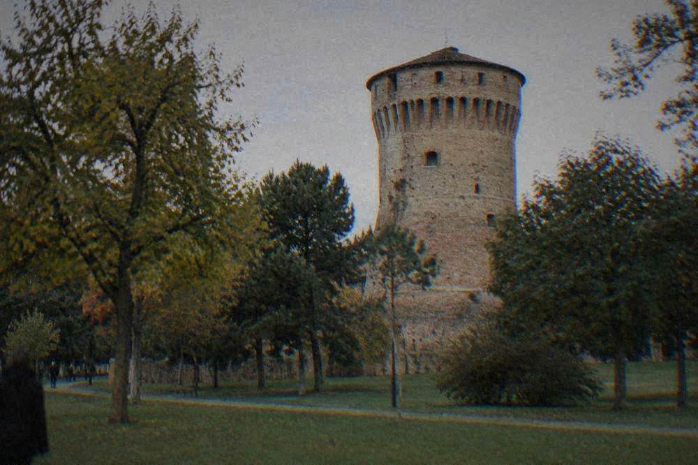 A round brick tower of a fortress rising above trees in a city park