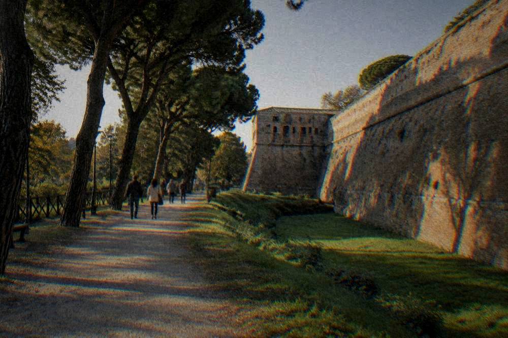 People strolling on a path beneath trees beside a fortress wall in Ravenna