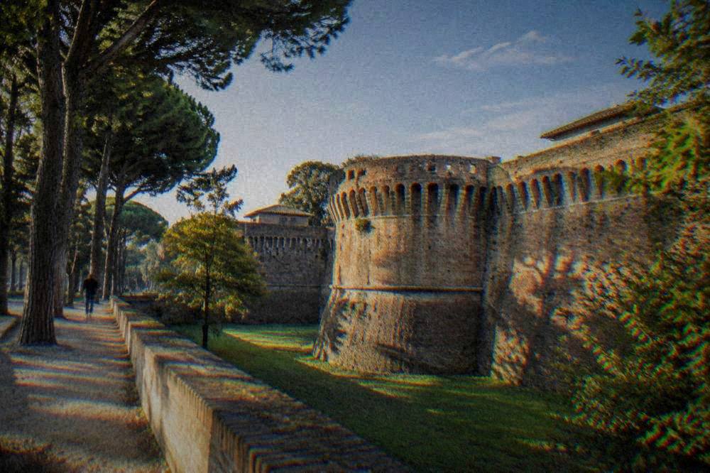 Sunlight falling across a fortress wall and trees in late afternoon in Ravenna