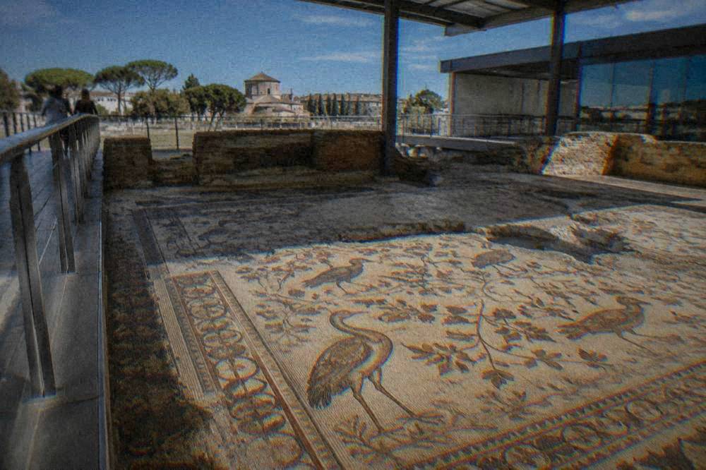 An excavated ancient floor mosaic with birds and floral motifs viewed from a walkway