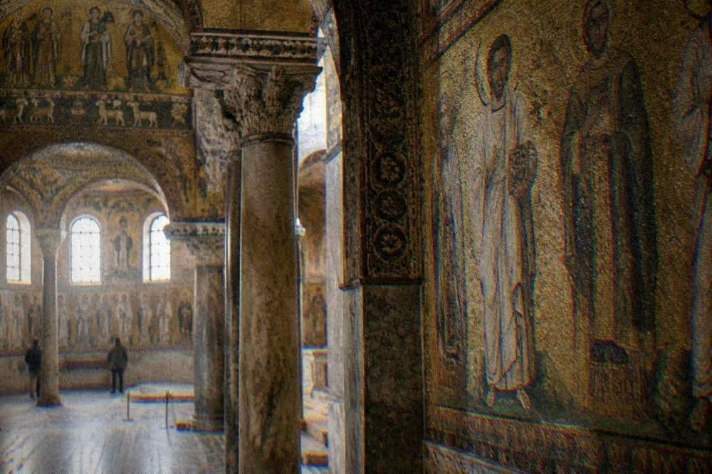 A golden Byzantine mosaic interior with saints and columns lit by soft daylight
