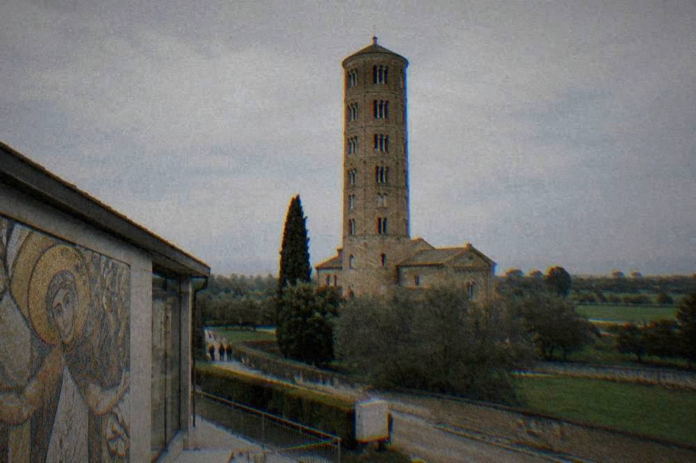 A tall brick basilica tower rising above flat green countryside near Ravenna
