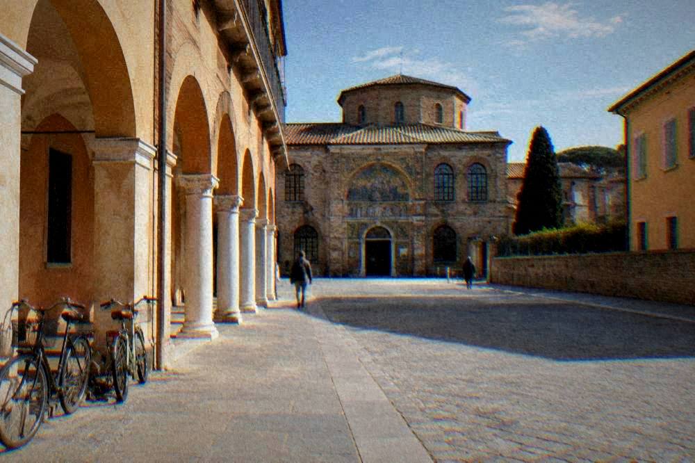 A quiet paved square in Ravenna with ochre facades, arcades and bicycles leaning on a wall