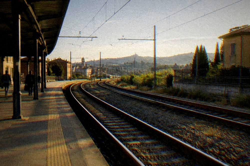 Train tracks curving away from a station toward the Emilia-Romagna countryside