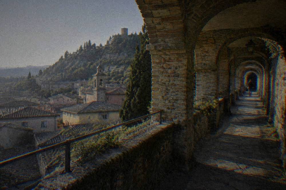 A narrow covered medieval walkway built into a cliff face with arched windows overlooking rooftops