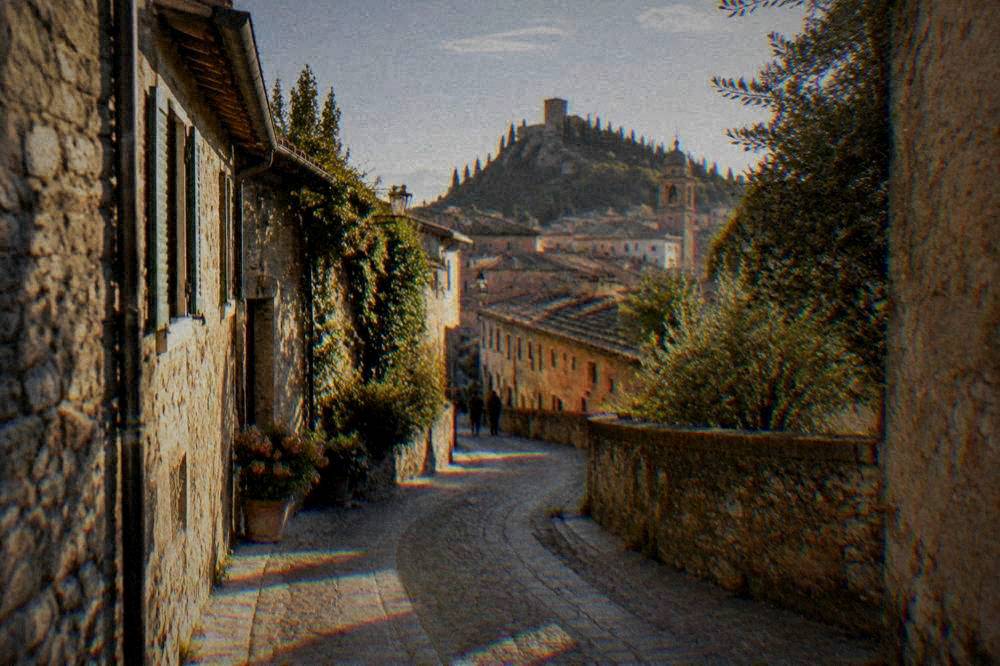 A stone village lane with small trattoria tables set out under arcades