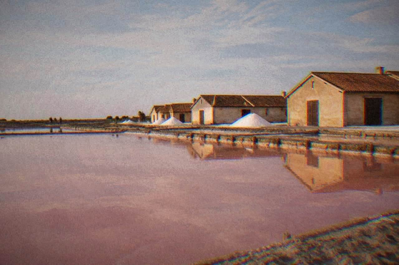 Salt pans at Cervia with pink water and a row of low salt warehouses under a wide sky