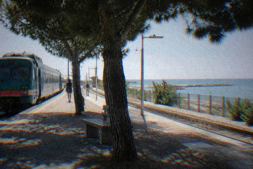 A regional train at a small Italian coastal station with the sea behind the platform