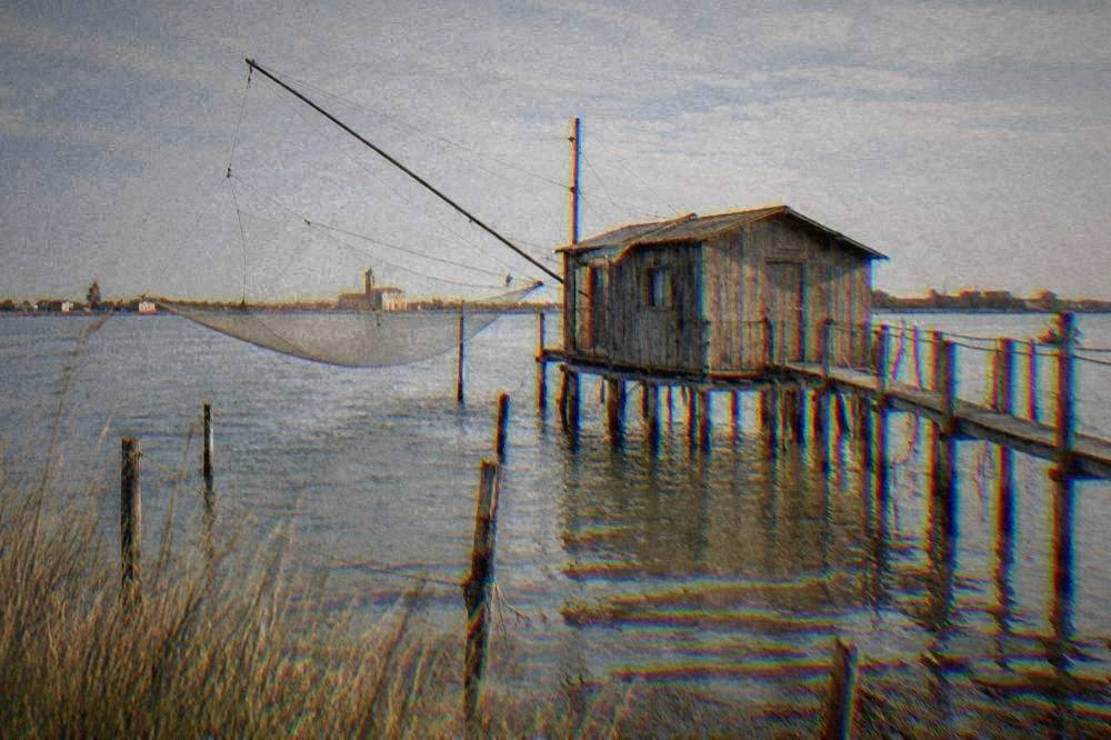 Weathered wooden fishing hut standing in the shallow lagoon water near Comacchio