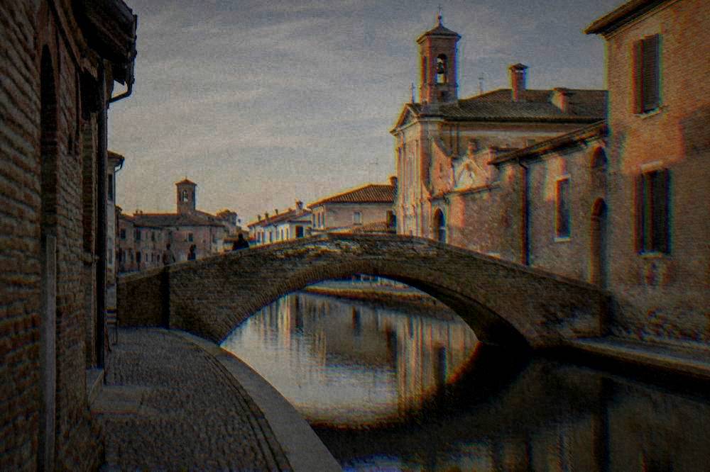 Arched stone footbridge over a Comacchio canal at late afternoon with warm light on brick walls