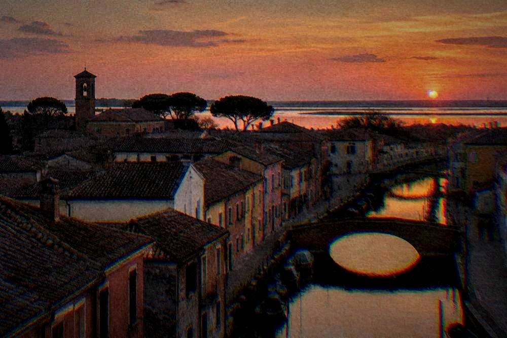 Wide view over Comacchio rooftops and canal water toward the flat lagoon horizon at dusk