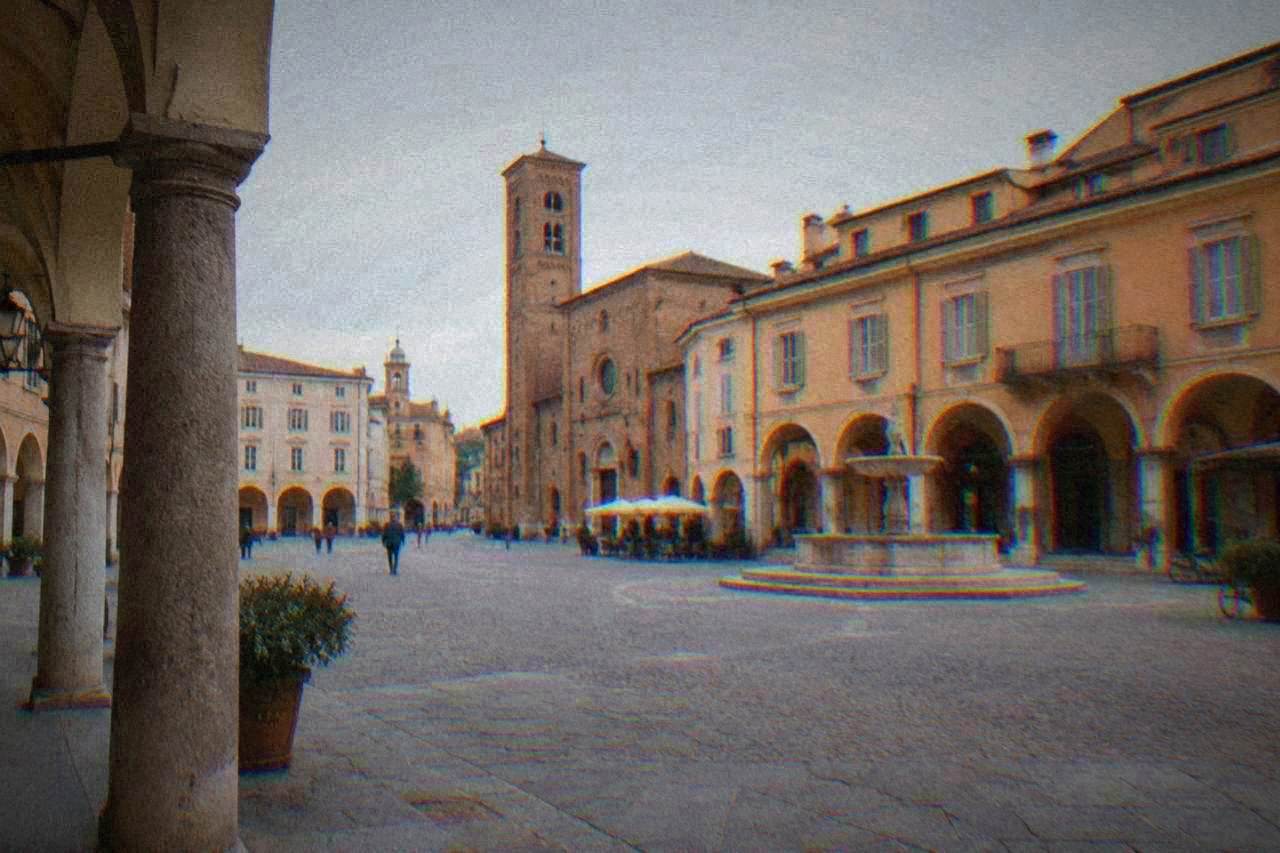 A quiet Italian town square with arcades and warm brick facades in late afternoon light