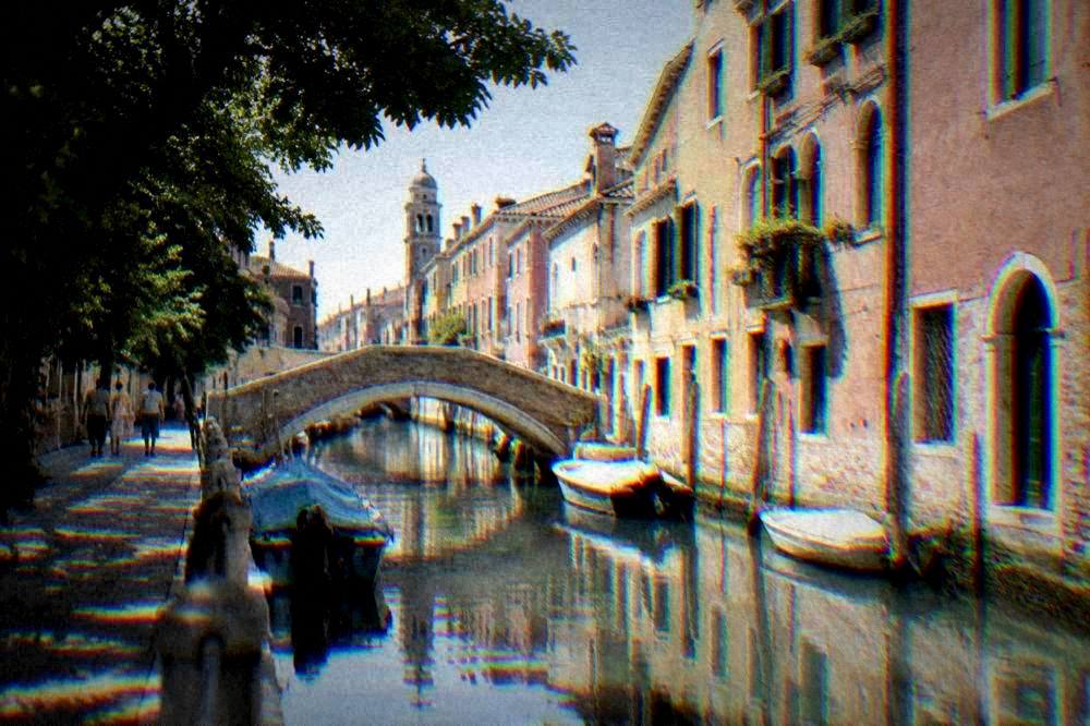 A small canal town with arched footbridges and pastel houses reflected in still water