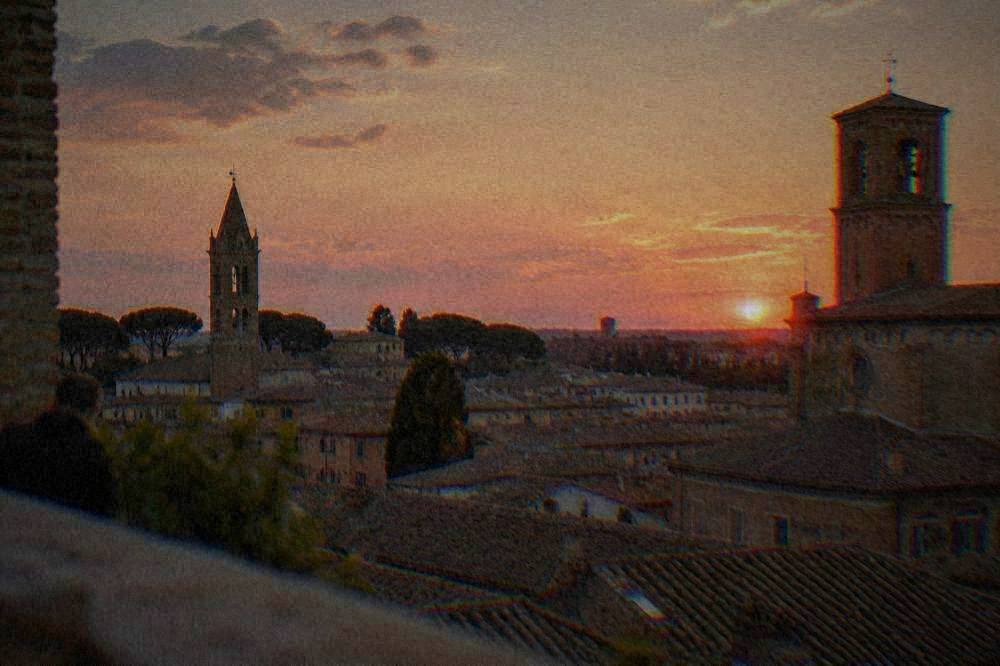 Sunlight over tiled rooftops and bell towers of an old Emilia-Romagna town at dusk