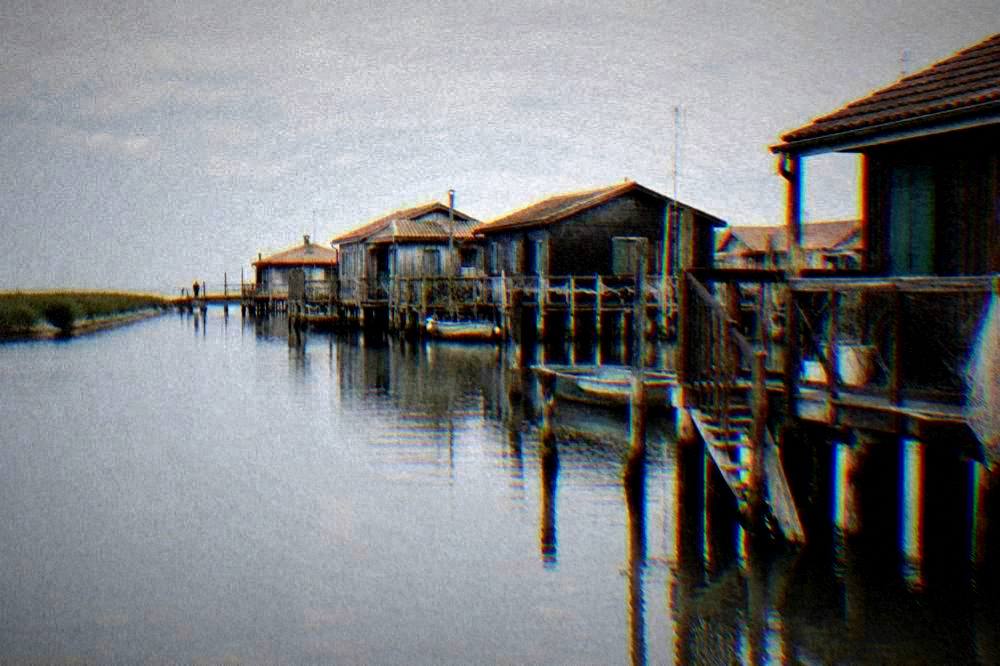 Row of wooden lagoon houses on stilts above calm water