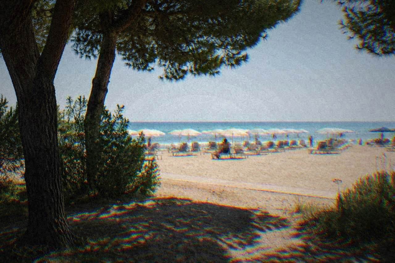 A wide sandy Adriatic beach with rows of sunbeds and a calm sea under a pale sky