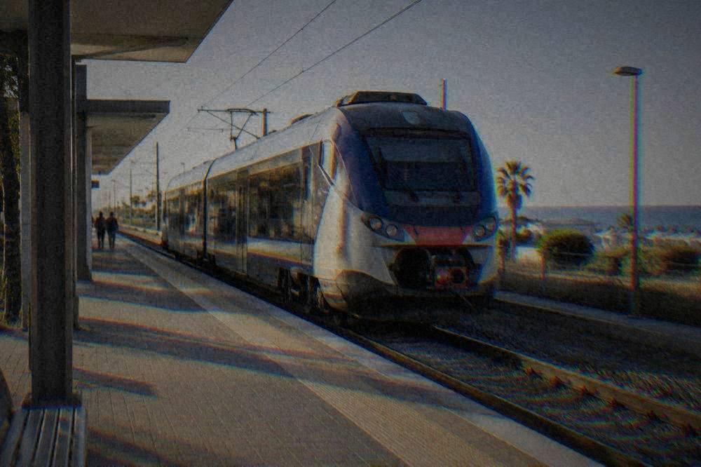 A regional train waiting at a small Italian station platform in morning light