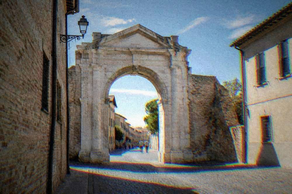 A pale stone archway standing over a cobbled street in an old Italian town
