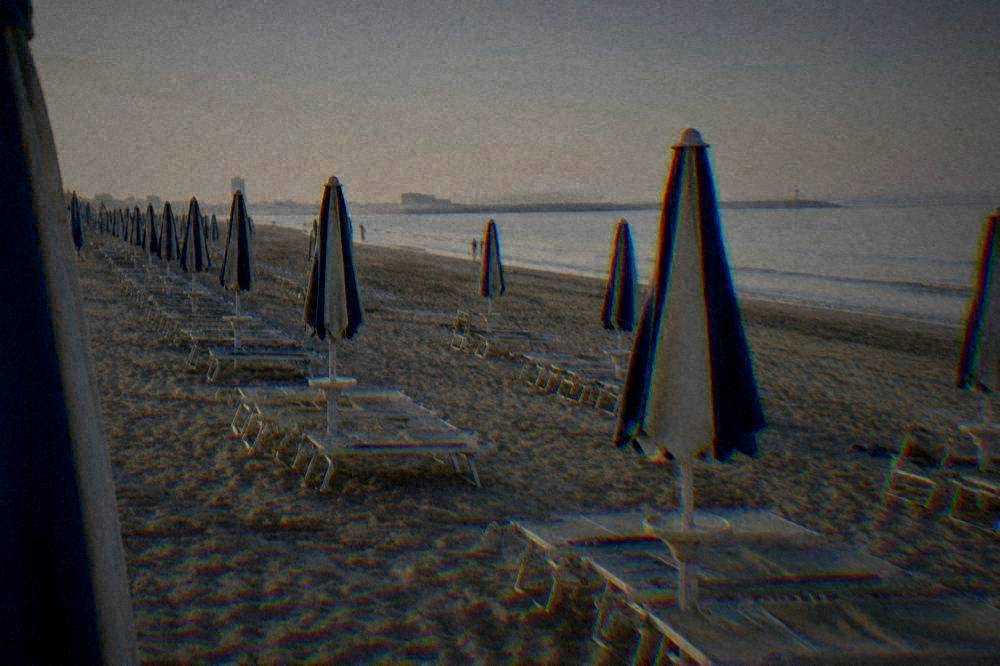 Sunbeds and umbrellas in neat rows on a wide sandy beach beside calm water