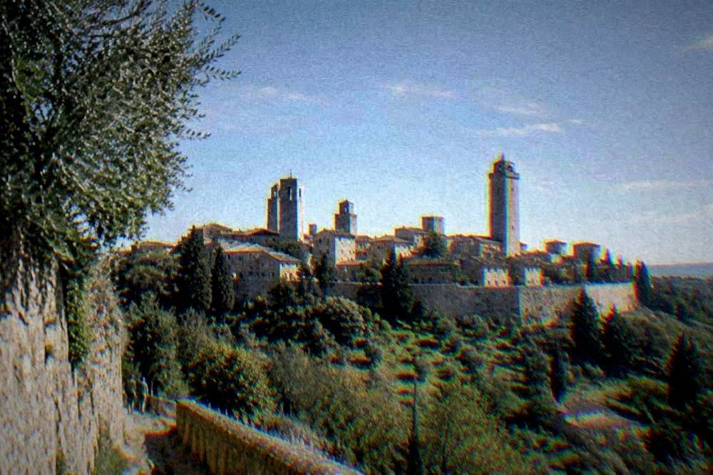 A walled hill town with stone towers rising above wooded slopes