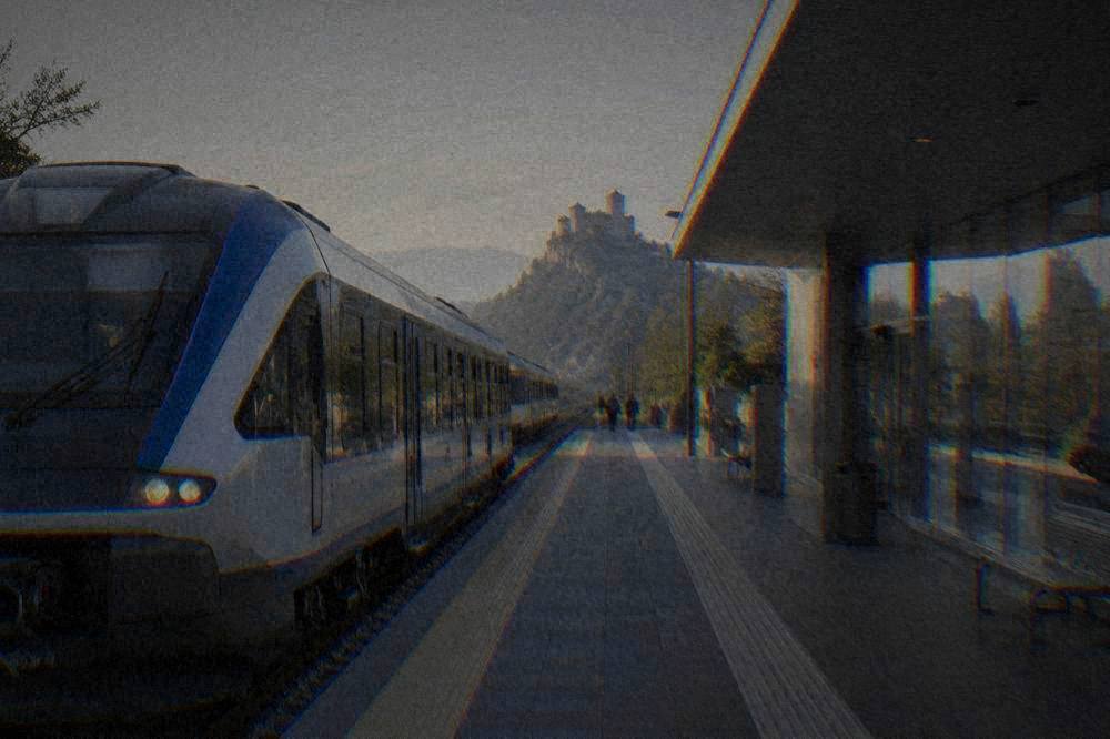A regional train waiting at an Italian railway station platform beside a modern station building