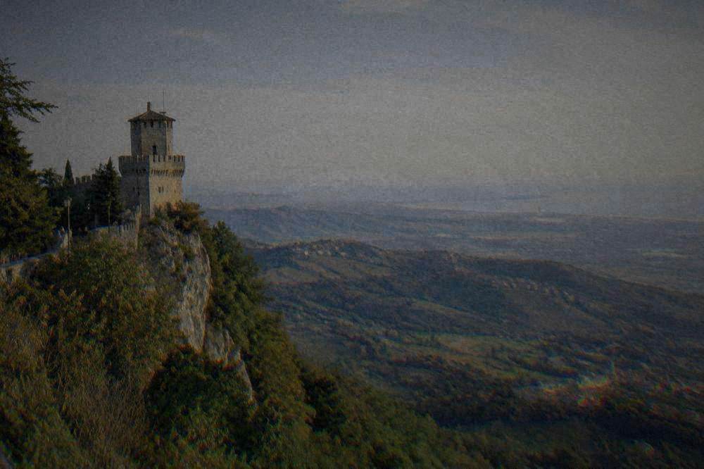 A stone guard tower on a green ridge with a wide view over rolling hills to a distant coastline