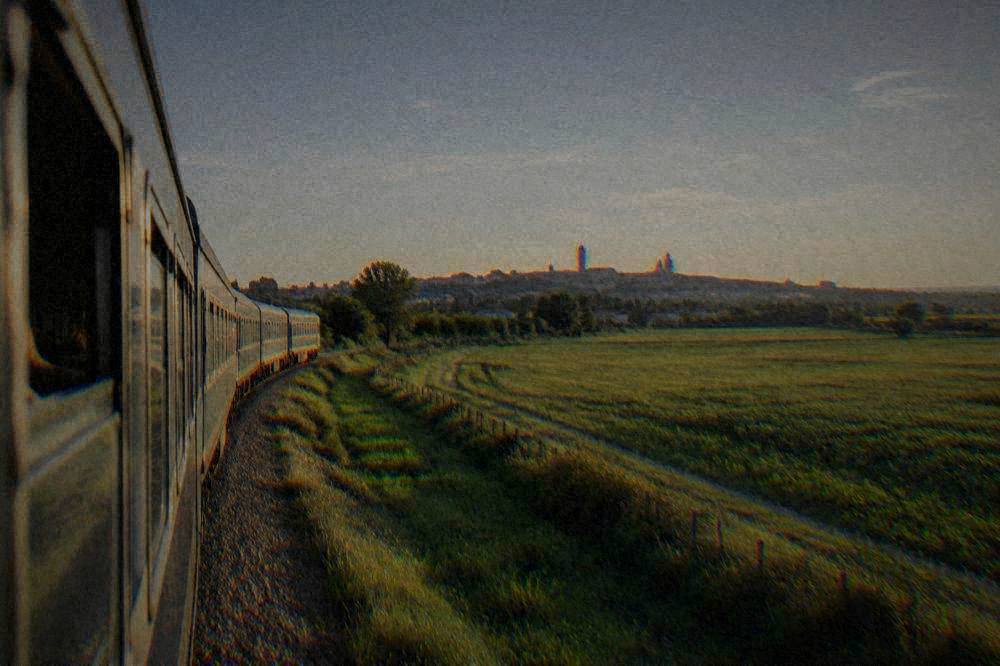 A passenger train travelling through flat green countryside toward a distant town