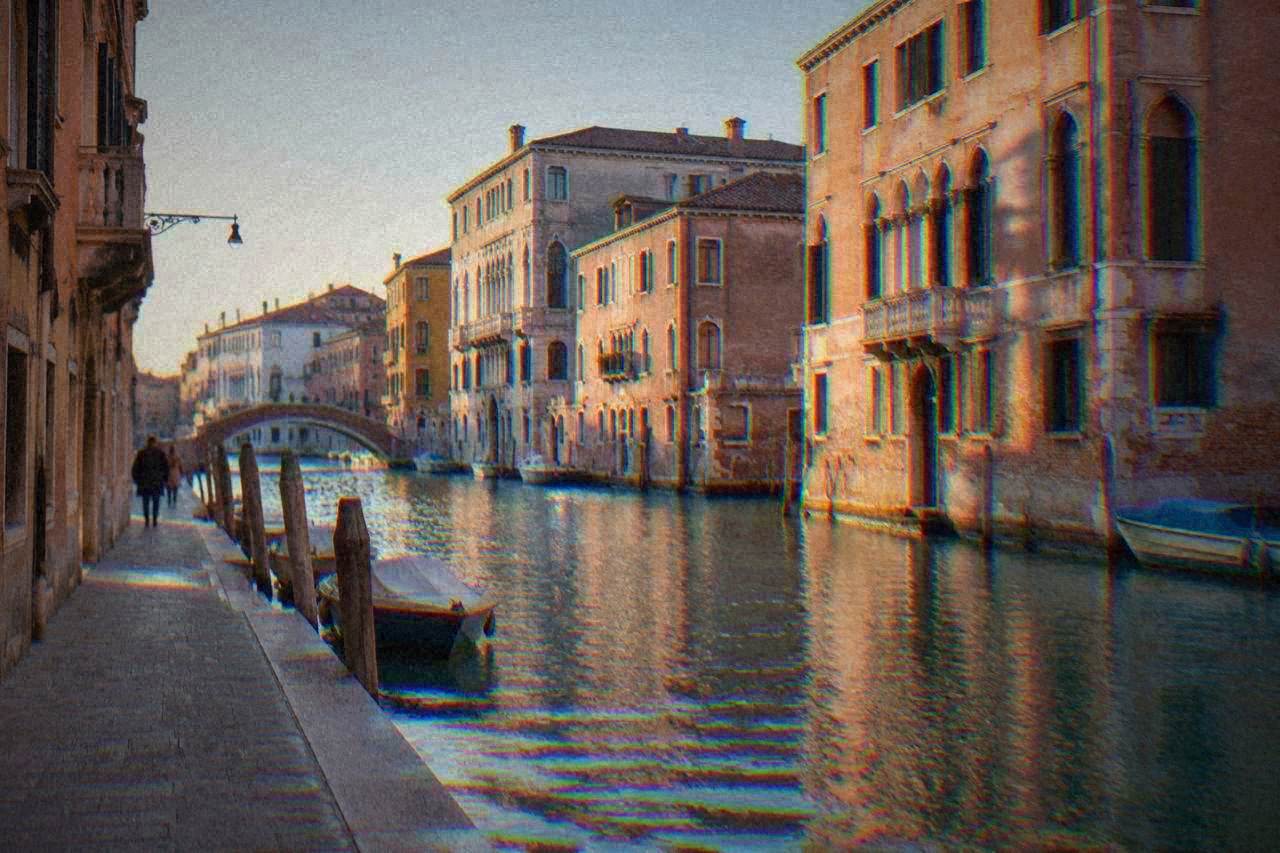 A canal in Venice with a stone bridge and moored boats along the water